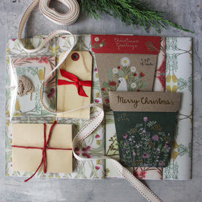 Gift wrapping items including a box, tag, and cards on a textured surface with greenery.