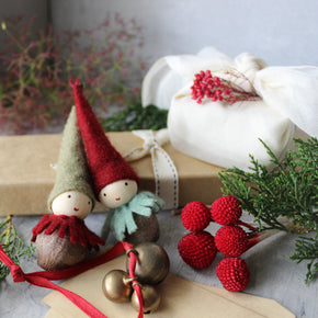 Two small figurines with red hats and green outfits next to a wrapped gift and red berries.