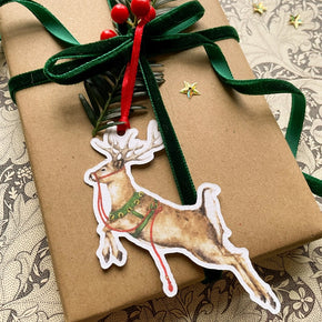 Gift wrapped in brown paper with a green ribbon and reindeer tag on a patterned surface.